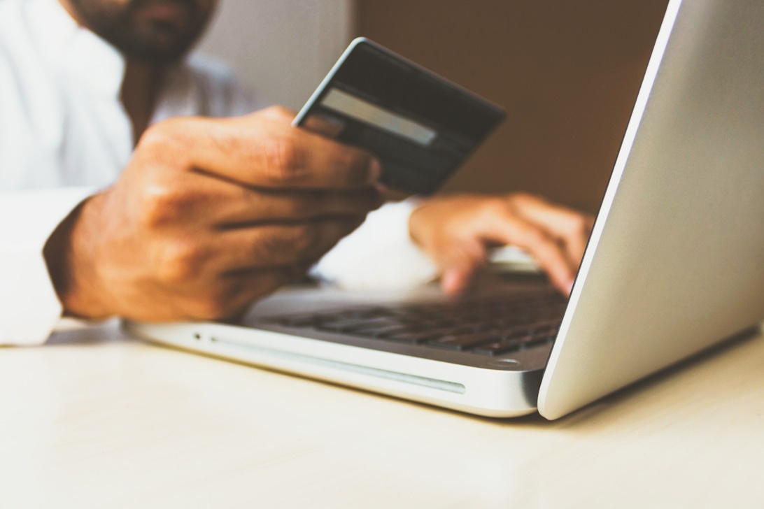 Händer som håller ett kreditkort och skriver på en bärbar dator, vilket illustrerar smidigheten med digitala finansiella transaktioner.