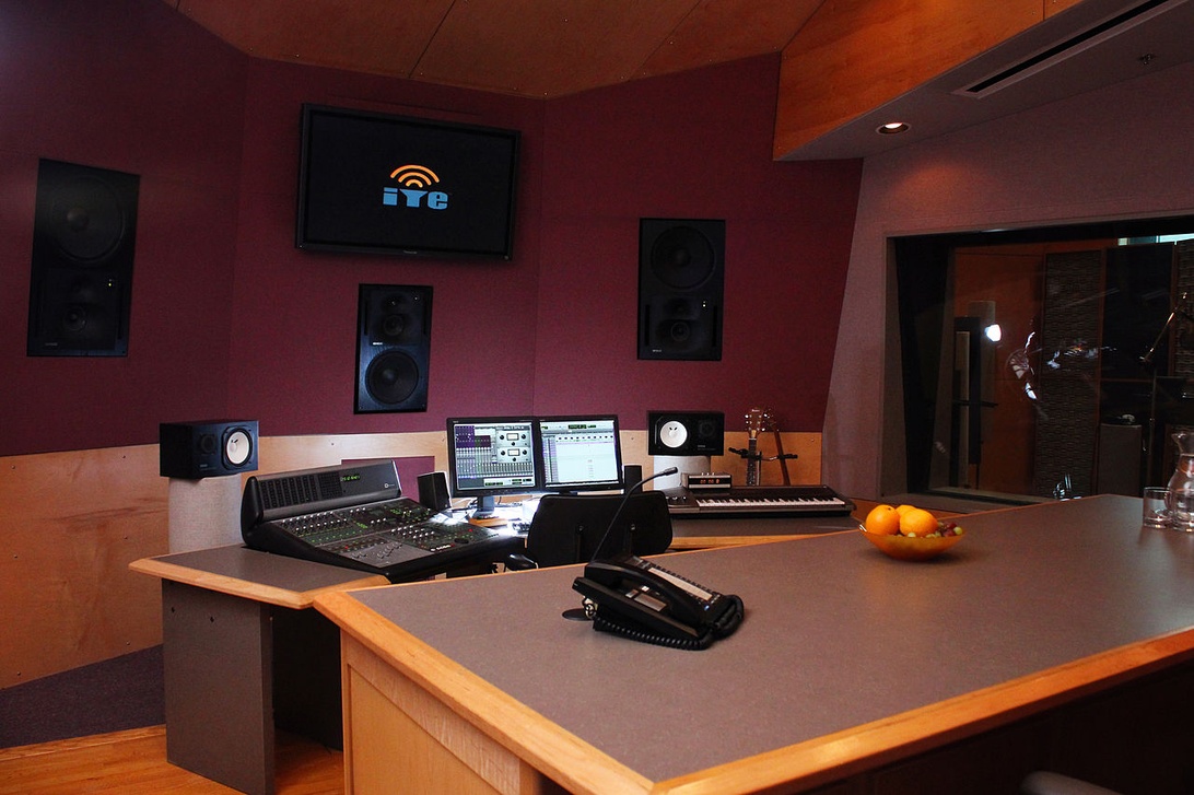 Ett kontrollrum i en professionell ljudstudio med mixerbord, flera datorskärmar och akustikbehandling på väggarna.