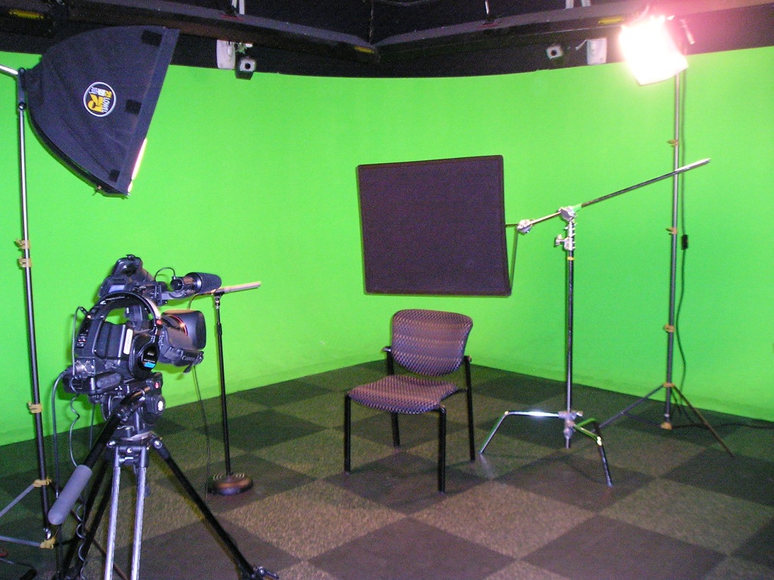 En professionell filmstudio med en biokamera på stativ, belysningsutrustning, bommikrofon och en stor grönskärm i bakgrunden.